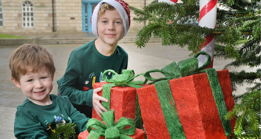 Two children holding presents beside a decorated Christmas tree